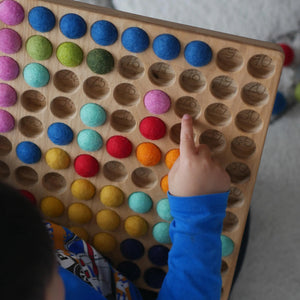 Kind rechnet mit Hunderterbrett mit bunten Filzkugeln